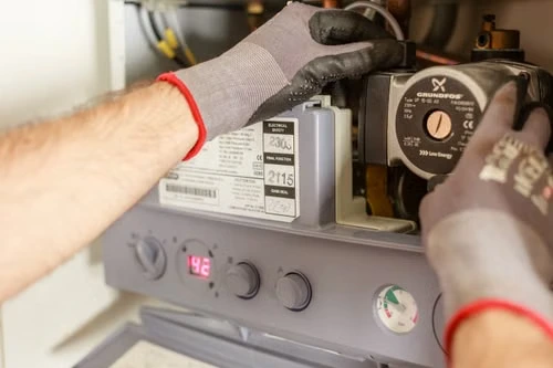 Professional technician's hands in work gloves performing appliance repair on a residential boiler pump.