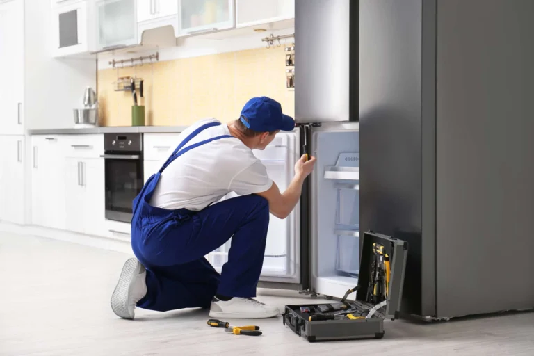Appliance repair technician inspecting a refrigerator's cooling system in a San Antonio kitchen